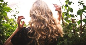 Blonde woman with curly hair surrounded by lush greenery, enjoying a sunny day.