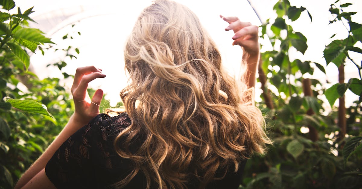 Blonde woman with curly hair surrounded by lush greenery, enjoying a sunny day.