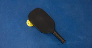 A pickleball paddle and ball on a textured blue surface, showcasing sports equipment.