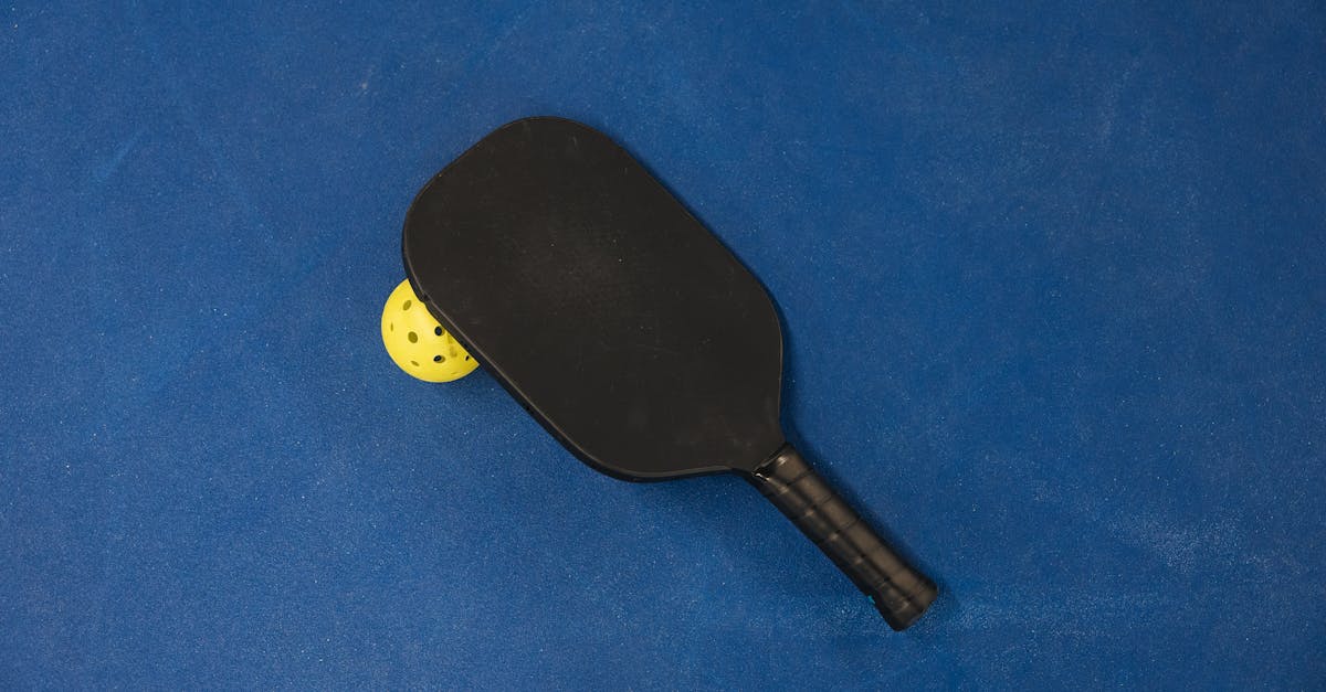 A pickleball paddle and ball on a textured blue surface, showcasing sports equipment.