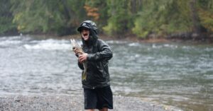 Boy celebrates catching a fish on a rainy day by the riverbank.