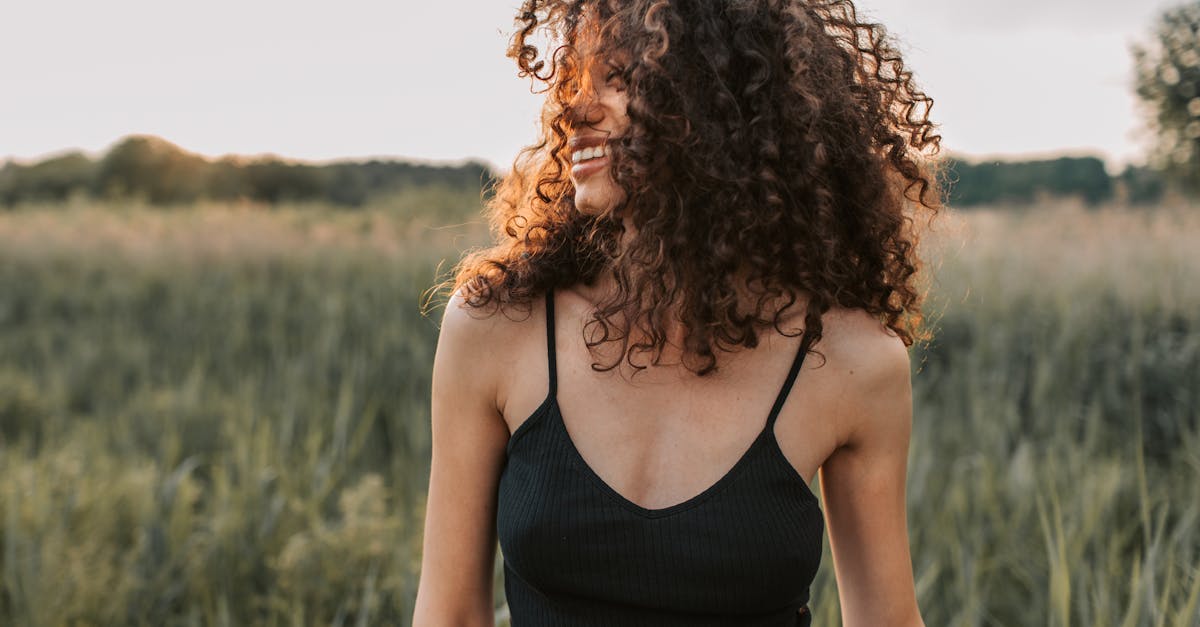 A cheerful woman in casual attire enjoying a sunny day outdoors with natural curly hair.