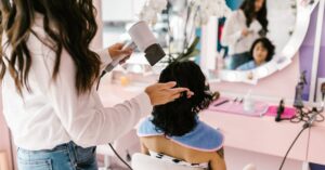 A hairstylist uses a hairdryer on a client at a modern salon with a mirror reflection.