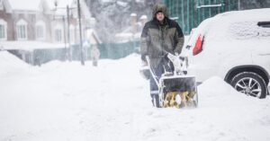 A man using a snow blower to clear snow from a snowy street during winter.