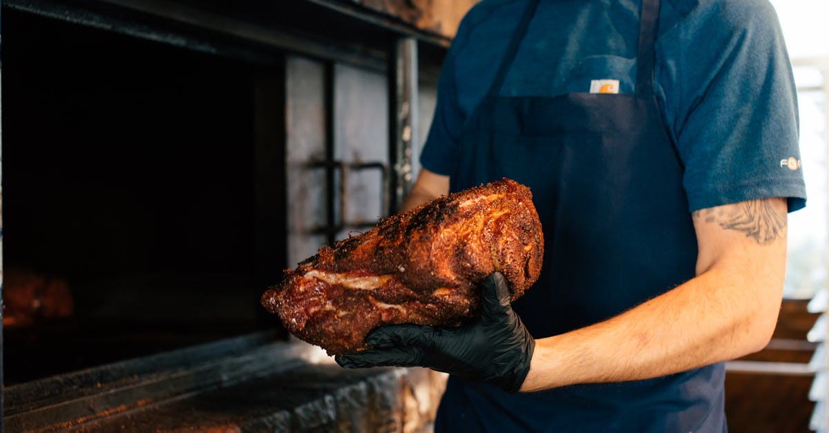 Chef holding seasoned meat with gloves near barbecue pit, cooking outdoors.