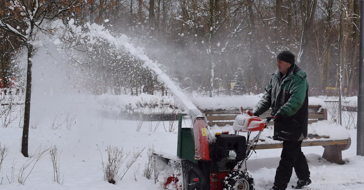 A man uses a snow blower in a snowy park during wintertime.