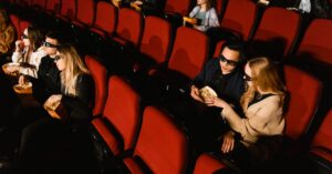 People in a theater wearing 3D glasses watching a movie with popcorn.